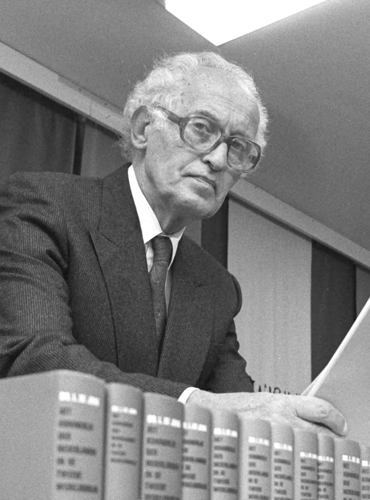 Loe de Jong achter een rij banden van zijn geschiedwerk, met zijn hand op de boeken.